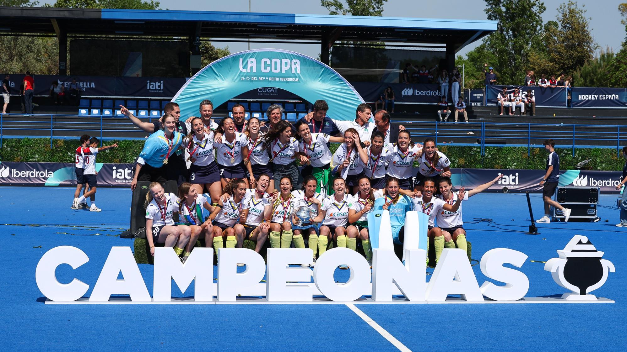 El equipo femenino RCCVM de hockey sobre hierba celebra su triunfo en la Copa delante de un cartel de campeonas. Foto: RFEH