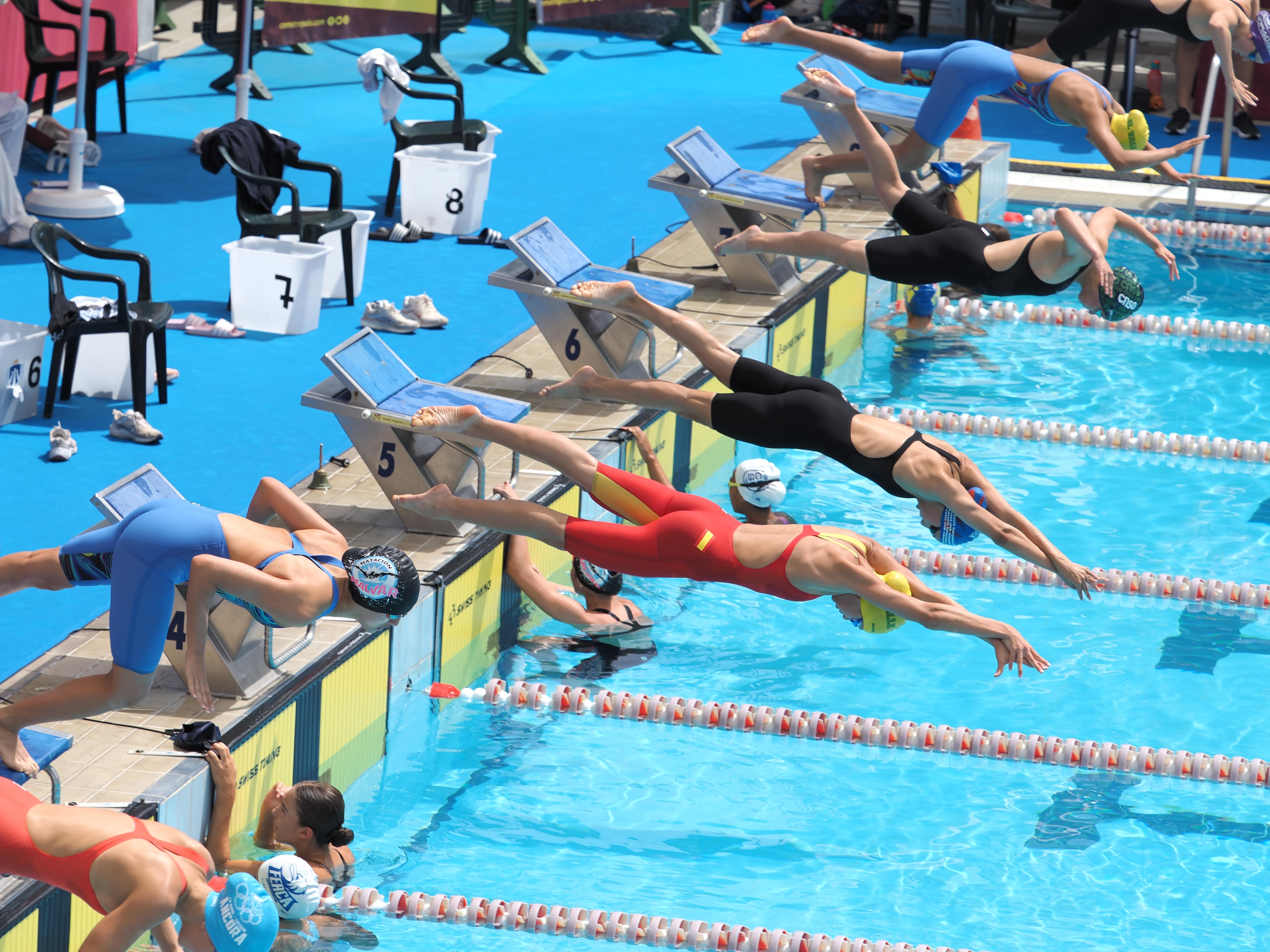 Lola Melgosa Ureña (bañador rojo) se lanza al agua en una de las pruebas del Campeonato de España infantil de verano.