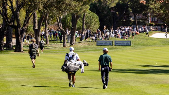 Un golfista y su caddie caminan por el Recorrido Negro de golf del Real Club de Campo Villa de Madrid.on las Torres de Madrid al fondo.