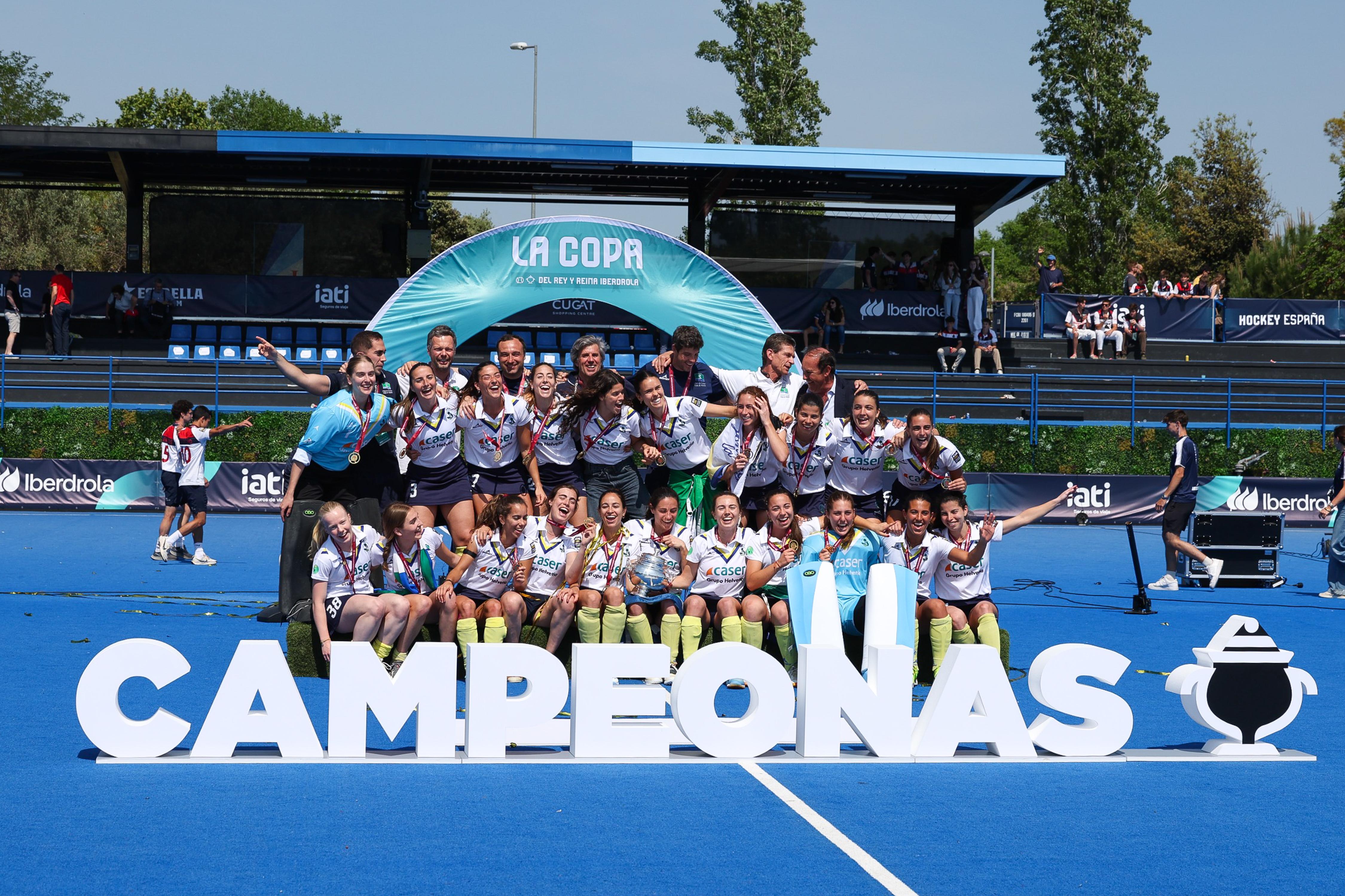 El equipo femenino RCCVM de hockey sobre hierba celebra su triunfo en la Copa delante de un cartel de campeonas. Fotos: RFEH