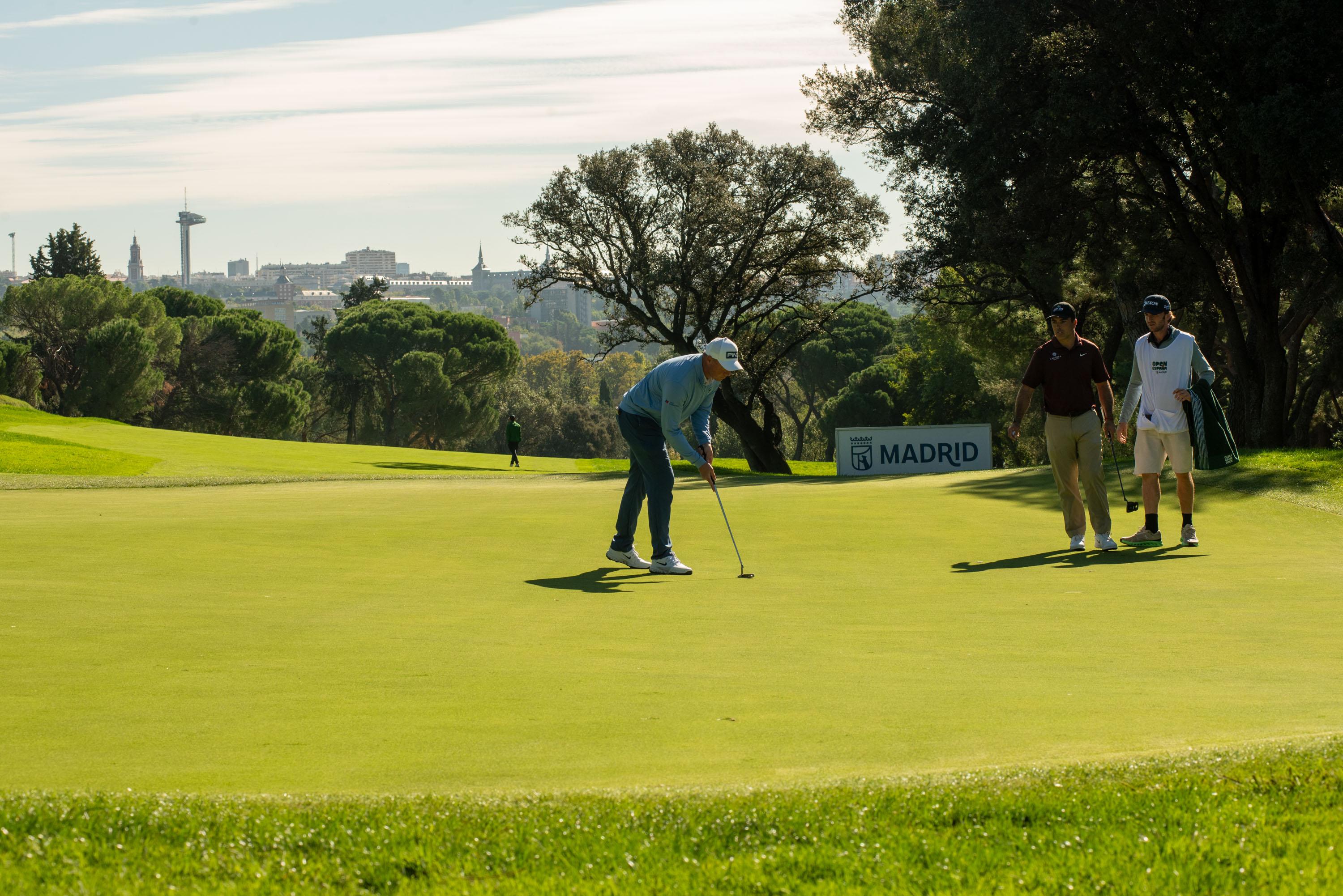 Un golfista repara un green, con el Faro de Moncloa al fondo.